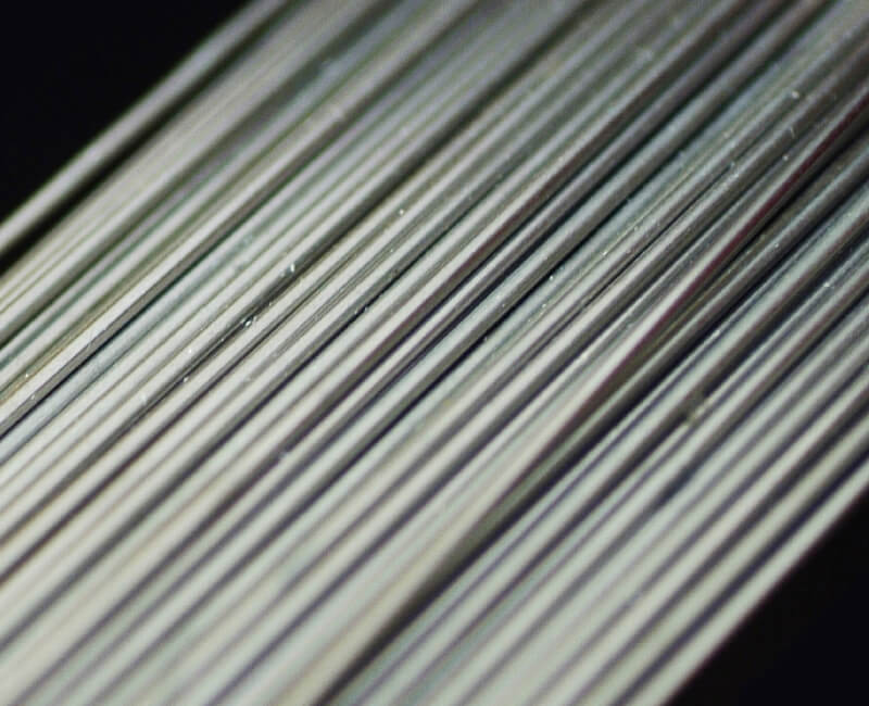 Close-up of thin alloy metal bars arranged in parallel with a reflective surface.