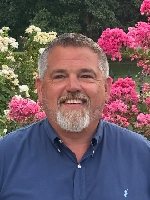 Portrait of Kyle Robinson smiling in front of vibrant pink and white flowers.