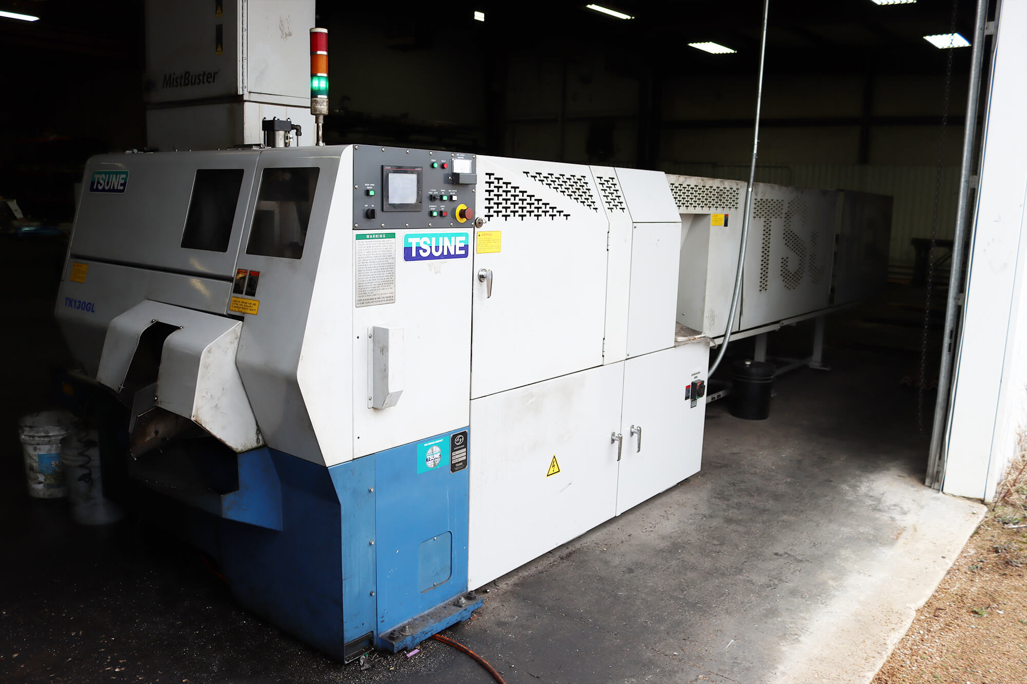 Large industrial TSUNE saw cutting machine, labeled TX130GL, in a factory setting.